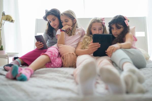 Four young girls focused on the cell phones and tablets in their hands
