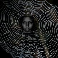 Woman's face peering from the center of a spider web