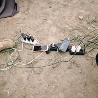 Cell phones with charger cables plugged into power bars on the ground outdoors