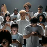 Group of young people wearing white t-shirts, all gazingat their cell phones