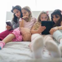 Four young girls focused on the cell phones and tablets in their hands