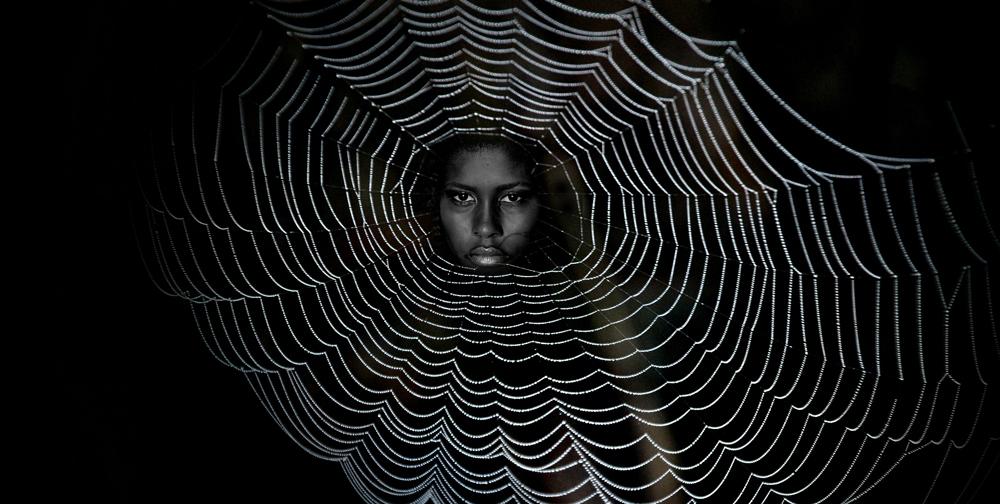 Woman's face peering from the center of a spider web