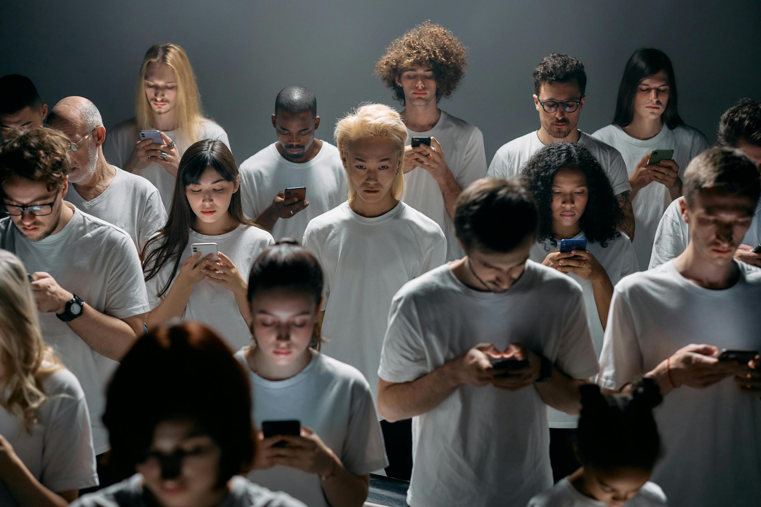 Group of young people wearing white t-shirts, all gazingat their cell phones